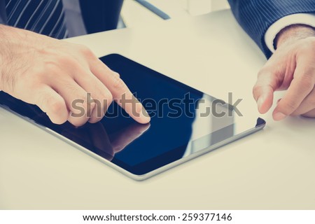 Businessman hand touching tablet pc screen on the table - vintage style color effect, tablet focused