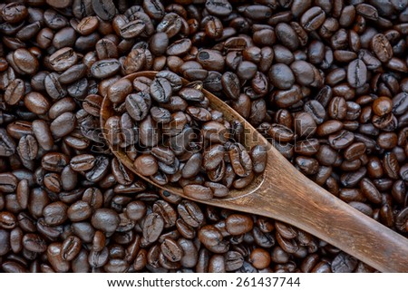 Spoonful of coffee beans on coffee bean heap - soft focus