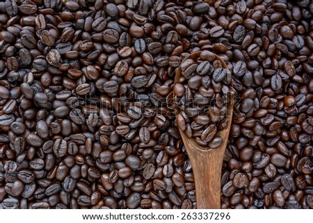 Spoonful of coffee beans on coffee bean heap - soft focus