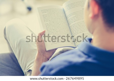 Young man reading book while sitting on the couch (over shoulder view) - vintage tone, soft focus