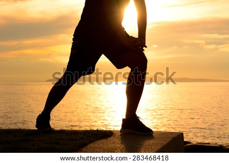 Silhouette of a man lower body, stretching at the beach in twilight