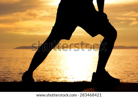 Silhouette of a man lower body, stretching at the beach in twilight
