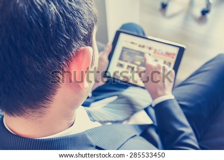 Businessman using tablet computer while sitting on the couch, over shoulder view, blurred screen - vintage tone