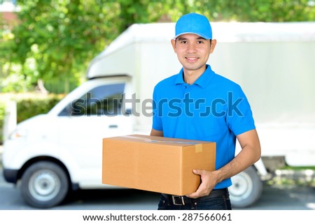 Deliveryman carrying a cardboard parcel box in front of delivery car