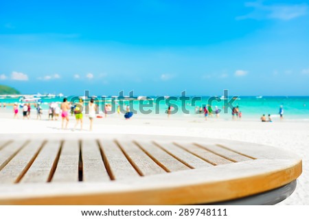 Round table top on blur beach background with people in colorful clothes - can be used for montage or display your products