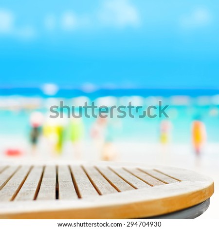 Round table top on blur beach background with people in colorful clothes - can be used for montage or display your products