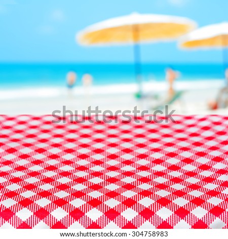 Red checkered picnic table cloth on blurred beach background, summer holiday background concept - can be used for display or montage your products