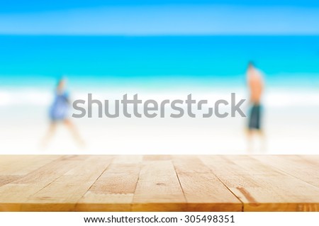 Wood table top on  blur background of two people playing at the beach - can be used for display or montage your products