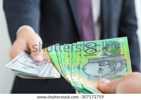 Money exchange and trading concept - hand holding Australian dollar (AUD) banknotes on blur background of businessman holding United States dollar (USD) bills,  about to swap