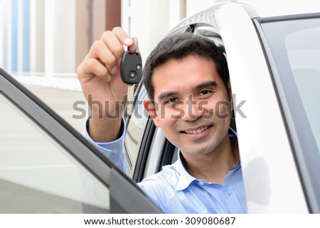 Smiling Asian man showing car key while sitting in a car (face focused)