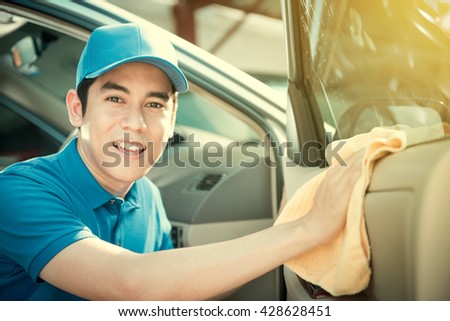 Smiling auto service staff cleaning car door - car detailing and valeting concept