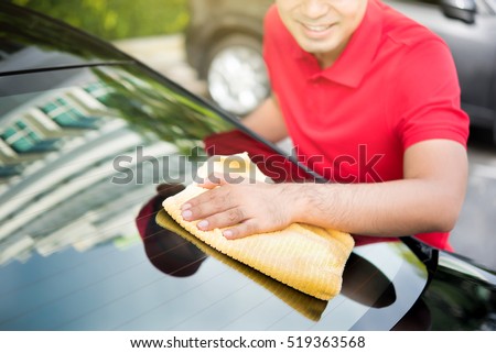 Auto service staff cleaning car rear windshield with microfiber cloth - car detailing and valeting concept