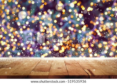 Wood table top with snow and bokeh from decorative light on Christmas tree in background - can be used for display or montage your products