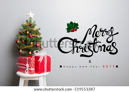 Gift boxes and small decorated Christmas tree on stool chair with MERRY CHRISTMAS and HAPPY NEW YEAR 2017 text on the wall