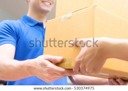 Delivery man in blue uniform handing parcel boxes to recipient - courier service concept