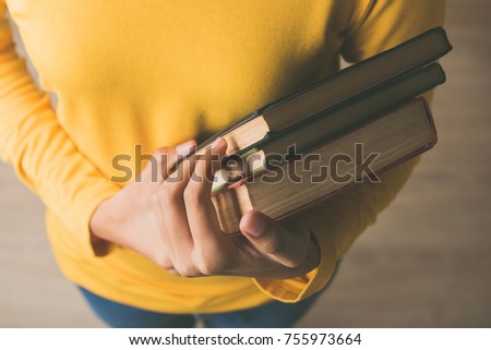 Hands of female student in yellow sweater carrying books in a library to study her class assignment research - education concept