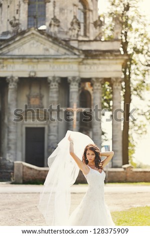 happy bride playing with veil next to old church