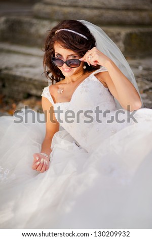 beautiful bride with sunglasses  sits on the steps  of the old church