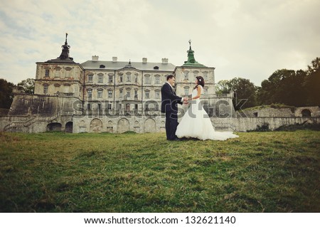 wedding, groom and bride holding hands next to old castle in west Ukraine