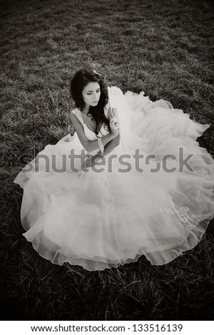 Bride sitting on the grass with fan, black and white