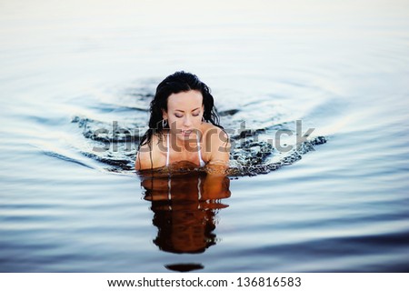 young  brunette woman swimming in lake, sunset light