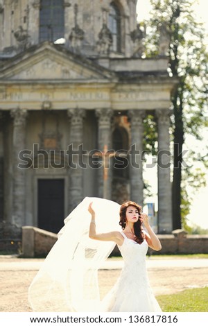 Gorgeous bride holding her veil next to old church