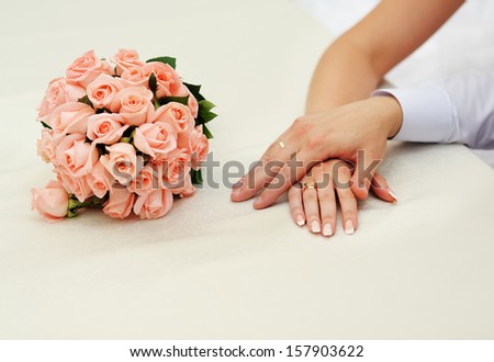 Hands of a newly wed couple. Pink roses wedding bouquet.