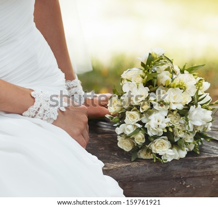 Bride sitting on bench holding wedding bouquet of various flowers.