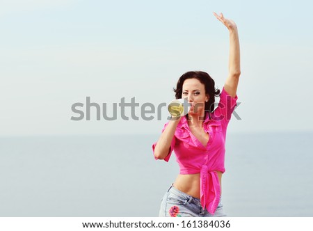 Young brunette woman in pink shirt with champagne bottle in hand  by the sea
