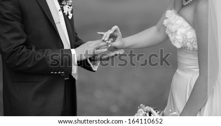 Bride puts a ring on finger of her groom. Picture in black and white. Togetherness.