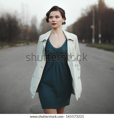 Woman with retro coiffure walking street wearing white coat.