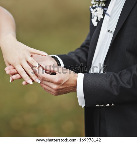 Hands of wedding couple putting golden rings to finger of each other.