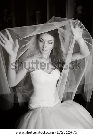 Young bride playing with veil, waiting for groom. Black and white wedding picture.
