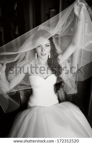 Beautiful young bride playing with veil, waiting for groom. Black and white wedding picture.