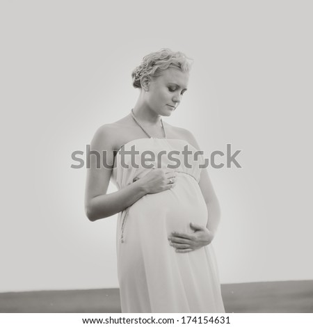 pregnant young woman in field, wearing white dress, black and white picture