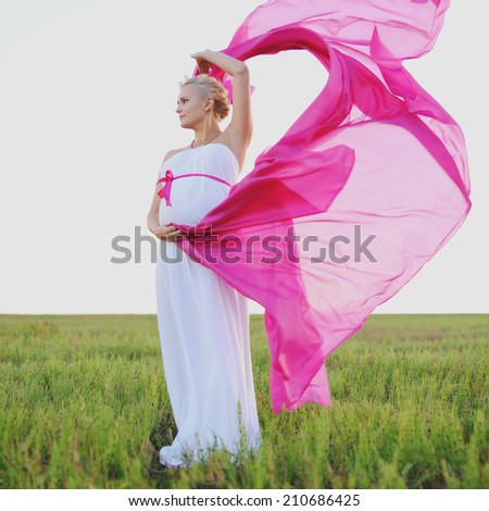 Young caucasian pregnant woman in a white greek dress with a pink bow at field.