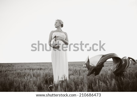 Young caucasian pregnant woman in a white greek dress at field.