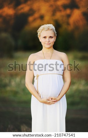 Portrait of  young pregnant woman in a white greek dress outside.