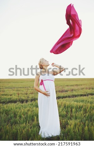 Portrat of  young pregnant woman in a white greek dress outside.
