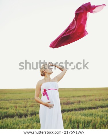 Portrat of  young pregnant woman in a white greek dress outside.