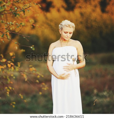 Young  caucasian pregnant woman in a white greek dress outside.