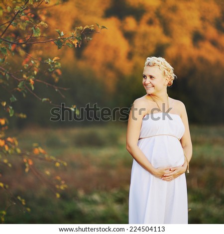 Young  caucasian pregnant woman in a white greek dress outside.