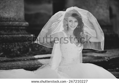 Black and white picture of young bride wearing wedding dress and posing on steps of old church.