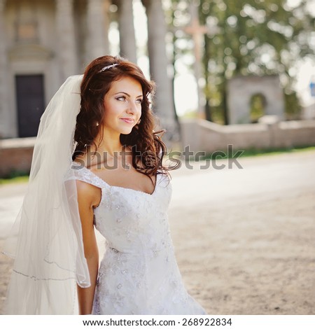 Young bride wearing wedding dress and posing outside against an old church.