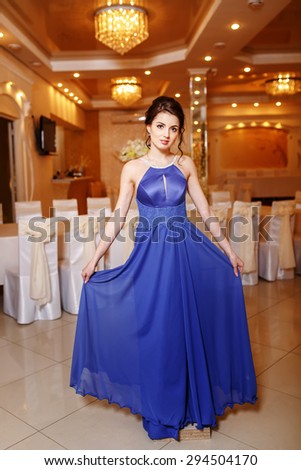 Interior portrait of young brunette woman wearing blue prom dress.