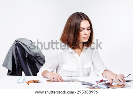 Young female office secretary working with papers while leaning on table with laptop. Charming brunette business woman.