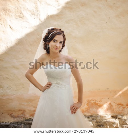 Young brunette bride next to old building wall. Summer wedding.