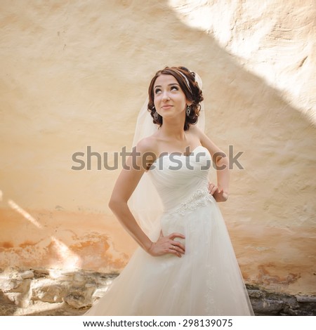 Young brunette bride next to old building wall. Summer wedding.