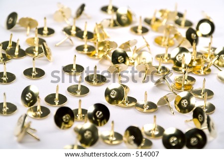 Brass thumb tacks scattered against a white background.