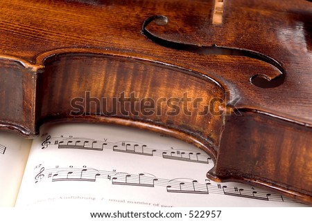 A dusty old violin rests sideways across a musical score. Only one line of the music is in focus.